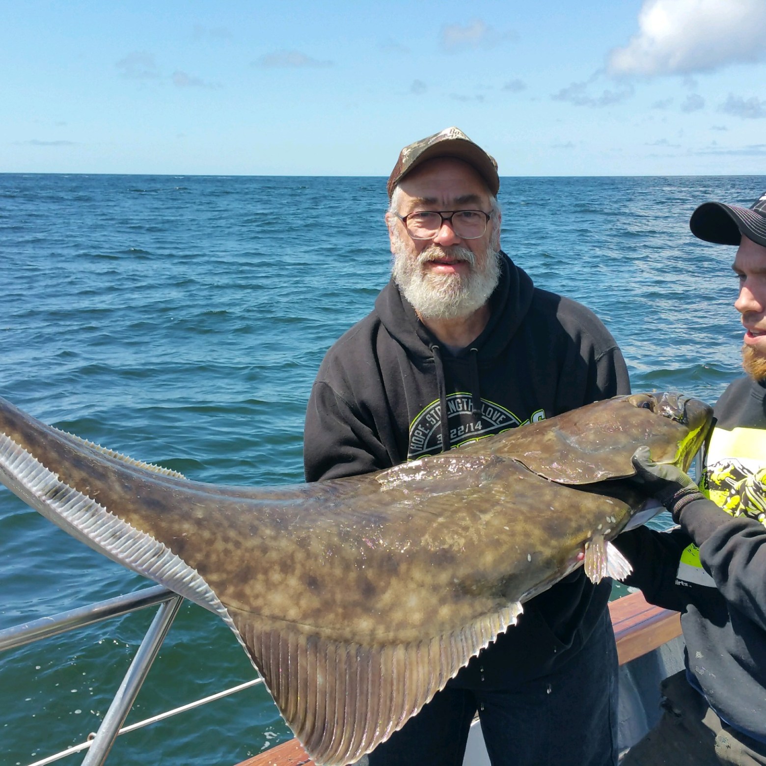 Three people on a boat holding a large fish over the ocean.