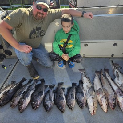 Man and boy on boat with rows of caught fish lined up on deck.