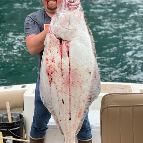 Smiling person holding a large, freshly caught fish on a boat with ocean background.