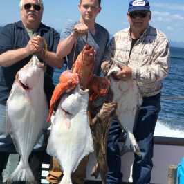Three men on a boat holding large fish with the ocean in the background.