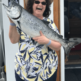 Person in hat holding a large fish, smiling on a boat.
