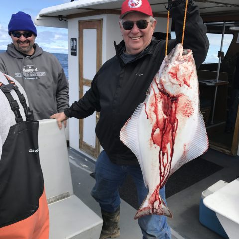 Man in sunglasses and red cap holding a large, bloody fish on a boat.