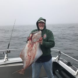 Person on a boat holding a large fish on a foggy day.