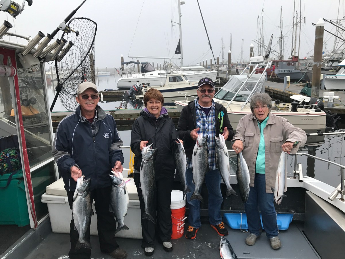 Four people on a boat holding freshly caught fish at a marina.