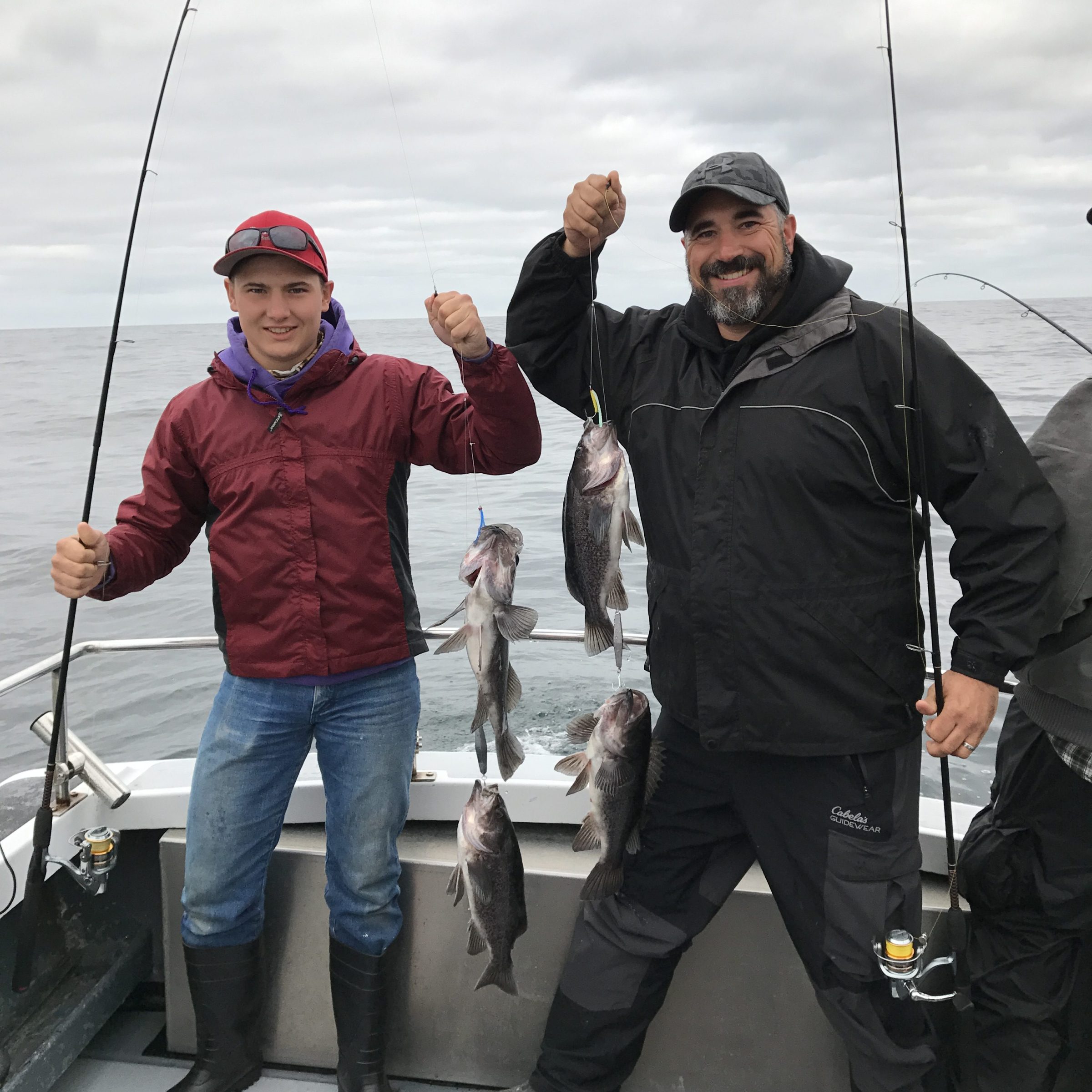 Two people on a boat holding fishing rods and several caught fish.