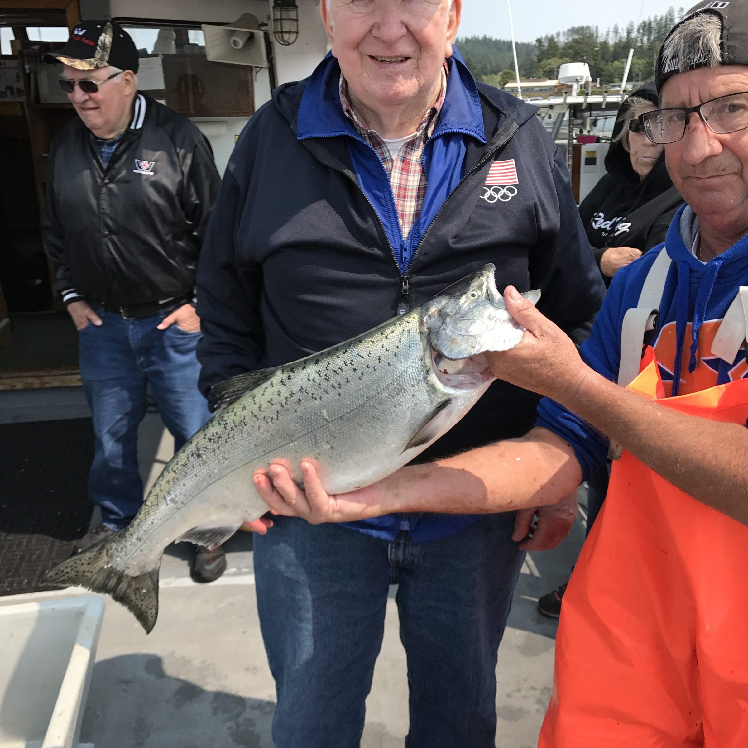 Older man holding a large fish on a boat with two others nearby.