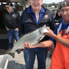 Older man holding a large fish on a boat with two others nearby.
