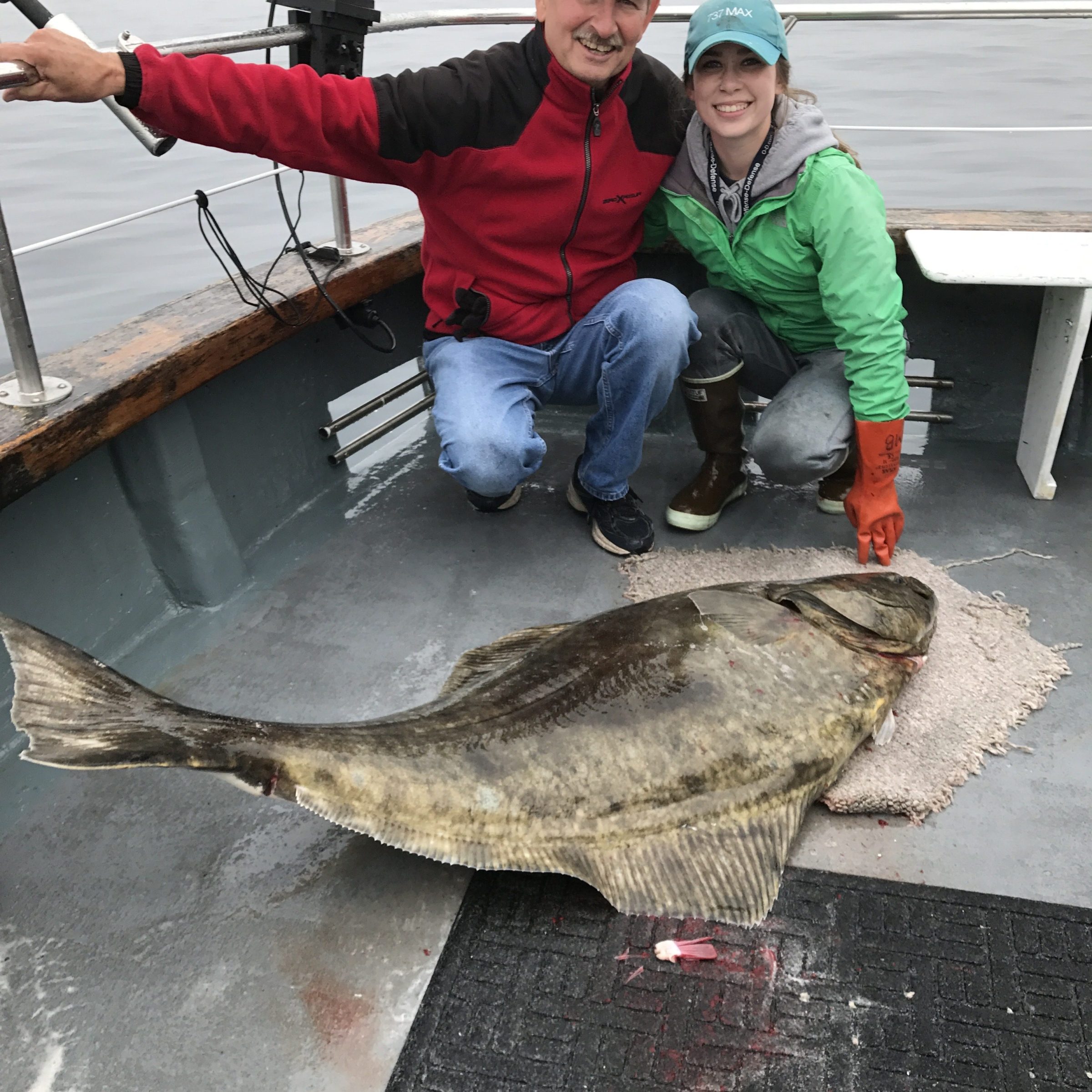 Two people on a boat kneel beside a large flat fish on the deck.