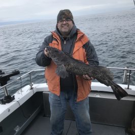 Person on a boat holding a large fish, with ocean in the background.
