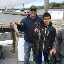 Two people on a boat holding caught fish, with a harbor in the background.