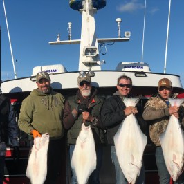 Group of six men holding large fish in front of a boat named Guardian.