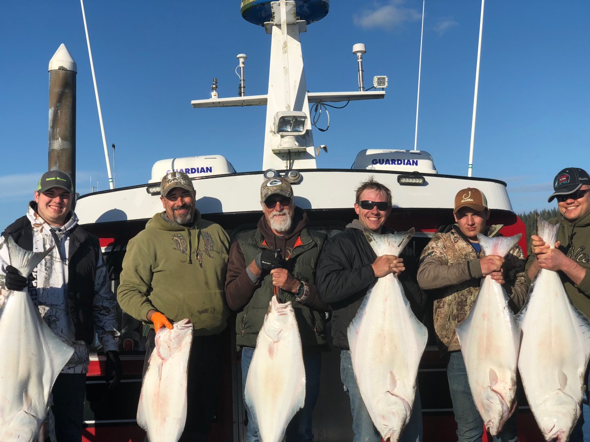 Group of six men holding large fish in front of a boat named Guardian.