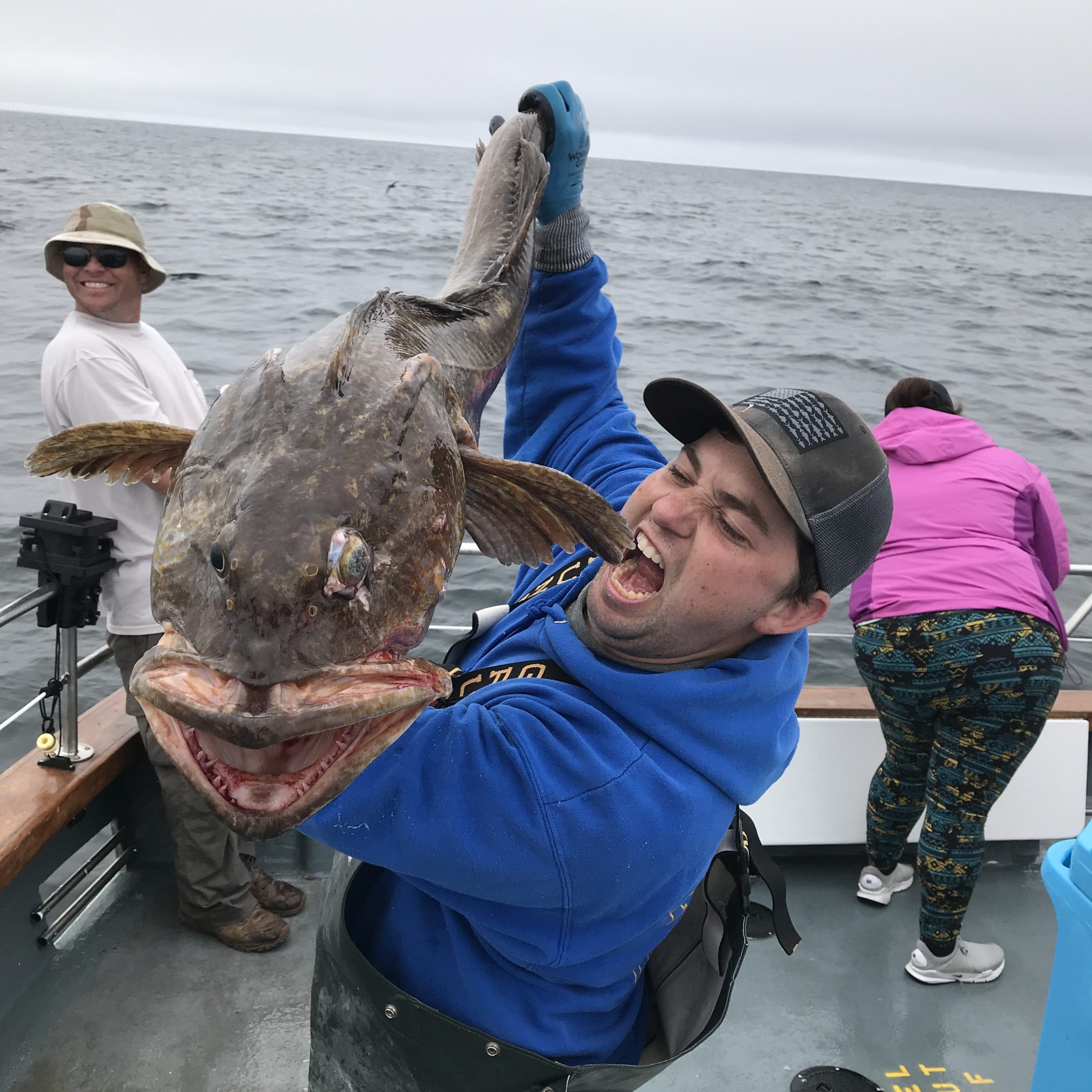 Man in blue jacket holds large fish on a boat, smiling.