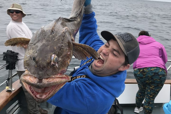 Man in blue jacket holds large fish on a boat, smiling.