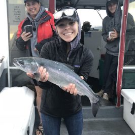 Smiling person holding a fish on a boat with two others in the background.