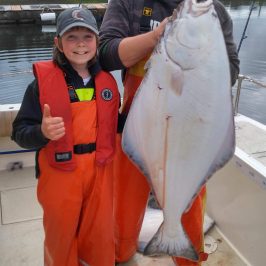 Two people in orange fishing gear holding a large fish on a boat.