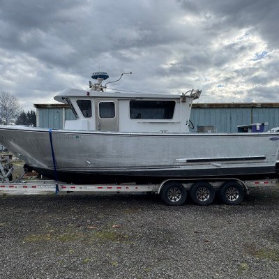 Silver cabin boat on a trailer with triple axles, cloudy sky background.