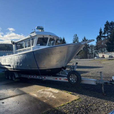 Large silver boat on a trailer in a sunny outdoor setting with trees in the background.